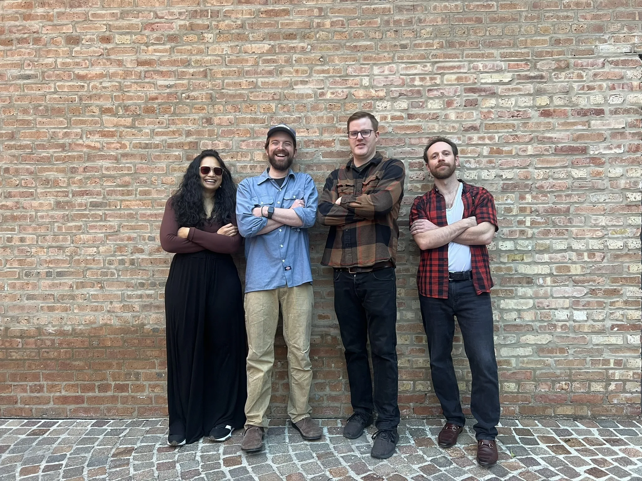 The four members of Potomac Bombs standing with arms crossed against a brick wall.